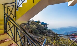 A staircase with metal railings leading to a building with a blue roof, surrounded by vegetation and mountains in the background. - Royal Suites Kasauli (Kasauli)