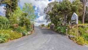 A paved road leading to a gated entrance surrounded by lush greenery and trees. - Riverside Lodge Paihia (Haruru)