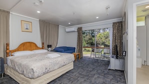 A hotel room with a large bed, a blue sofa, a small table, and a balcony with a chair. - Riverside Lodge Paihia (Haruru)