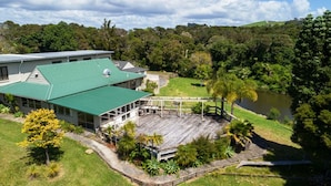 A large building with a green roof, a wooden deck, and a lake in the background. - Riverside Lodge Paihia (Haruru)