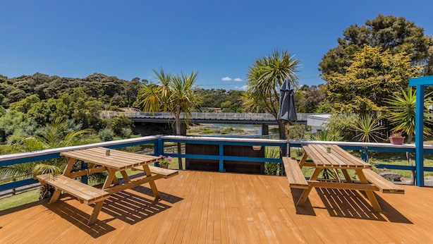 A wooden deck with picnic tables and a railing overlooking a river and greenery. - Riverside Lodge Paihia (Haruru)