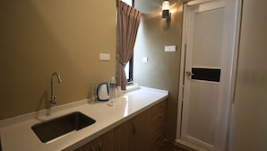 A kitchen with a sink, countertop, and cabinets. There is a window with curtains, a wall-mounted light, and a door. - Shamrock Greenhill (Ipoh)