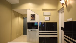 A hotel room with a bed, a TV mounted on a wooden panel, a black and white striped cabinet, and a wall-mounted light fixture. - Shamrock Greenhill (Ipoh)