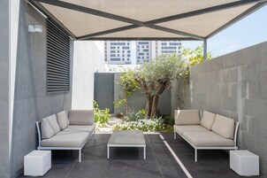 Un espacio exterior con dos sofás y una mesa de centro, rodeado por un muro bajo y un árbol.