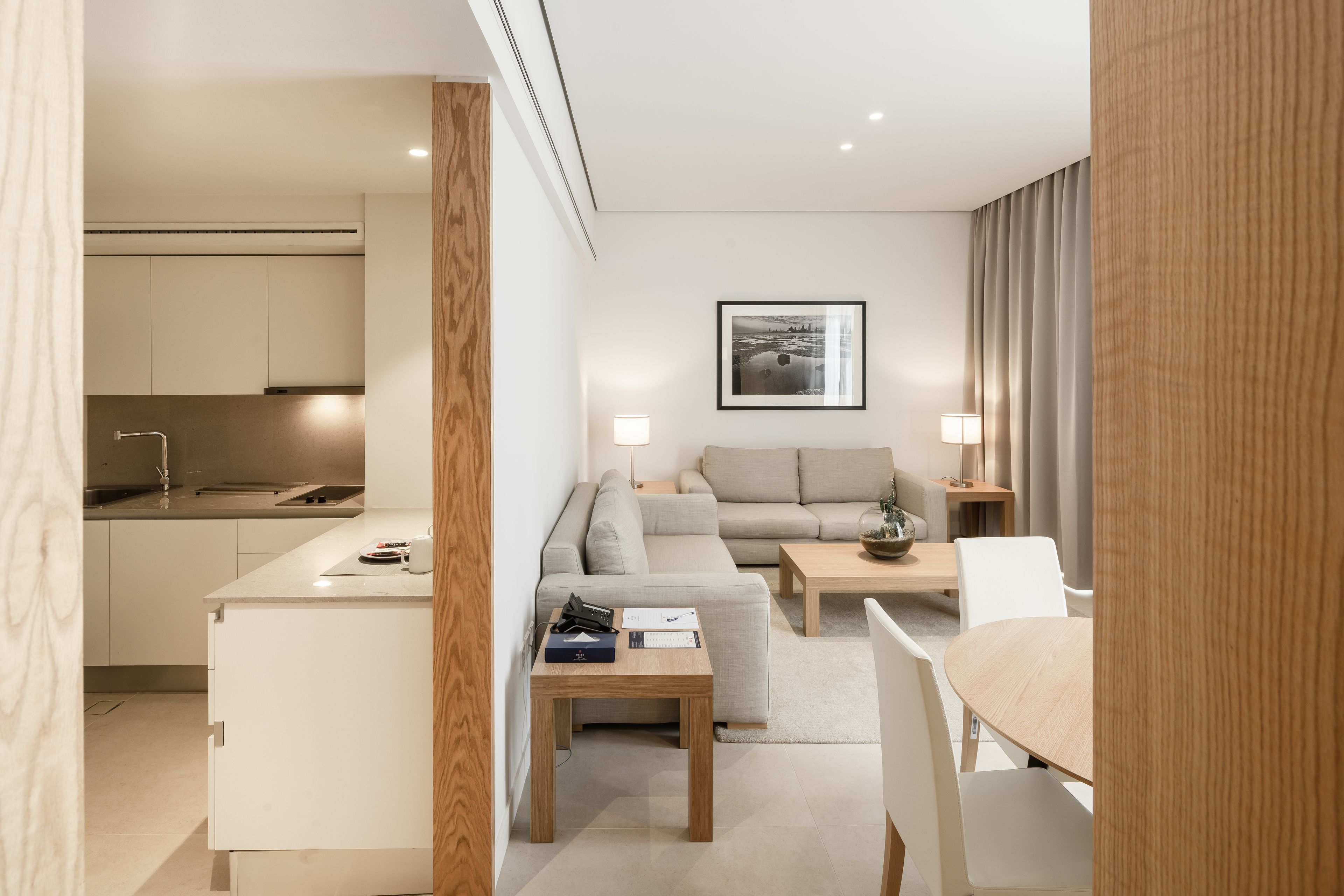 A modern hotel room with a kitchenette, a sofa, a dining table, and a coffee table.