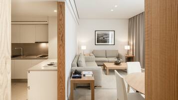 A modern hotel room with a kitchenette, a sofa, a dining table, and a coffee table.