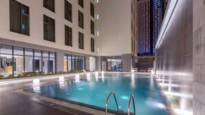 En indendørs swimmingpool med krystalklart vand, omgivet af en moderne bygning med store vinduer og flisegulv.