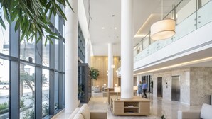 En moderne lobby med store vinduer, en receptionsdisk, siddeområder og en glasgelænder med udsigt til gaden.