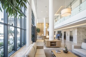 Un lobby moderno con grandes ventanales, un mostrador de recepción, zonas de estar y una barandilla de cristal con vistas a la calle.