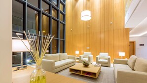 En moderne hotellobby med en trævæg, store vinduer og et siddeområde med sofaer og et sofabord.