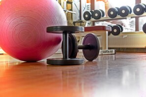 A gym with a pink exercise ball, a barbell, and weight plates on a wooden floor.