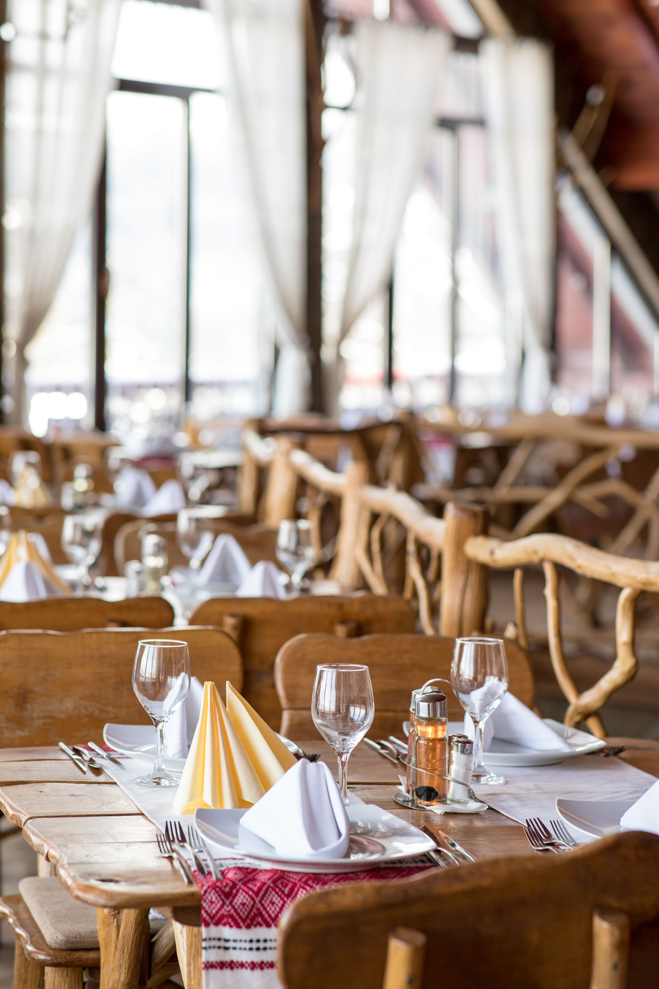 Een restaurant met houten tafels en stoelen, keurig gedekt met witte tafelkleden, servetten en bestek.