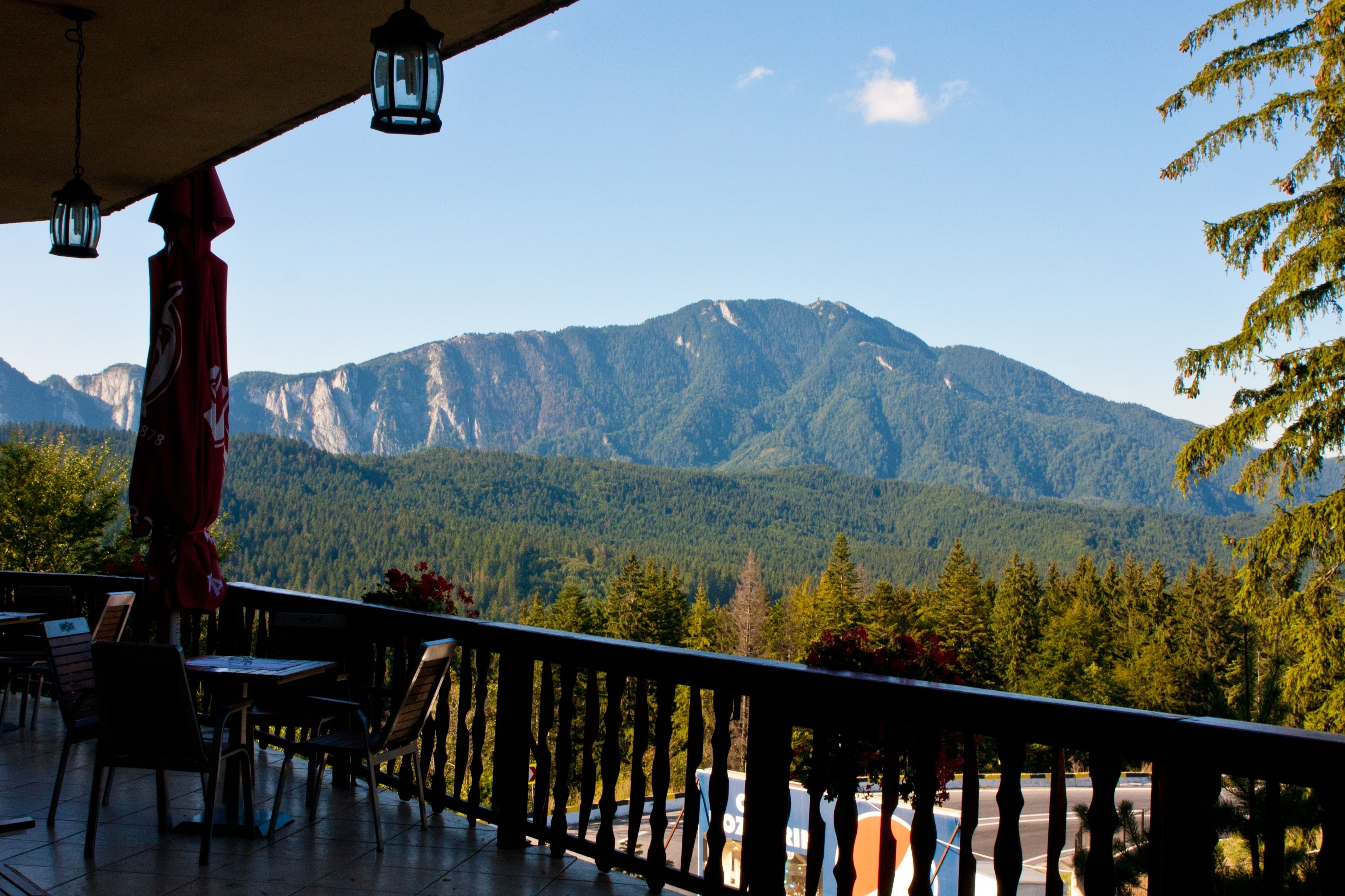 A terrace with a view of mountains, wooden furniture, and hanging lanterns.
