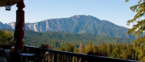 A terrace with a view of mountains, wooden furniture, and hanging lanterns.