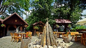Un espacio al aire libre con mesas y sillas de madera, rodeado de muros de piedra y estructuras de madera rústica.