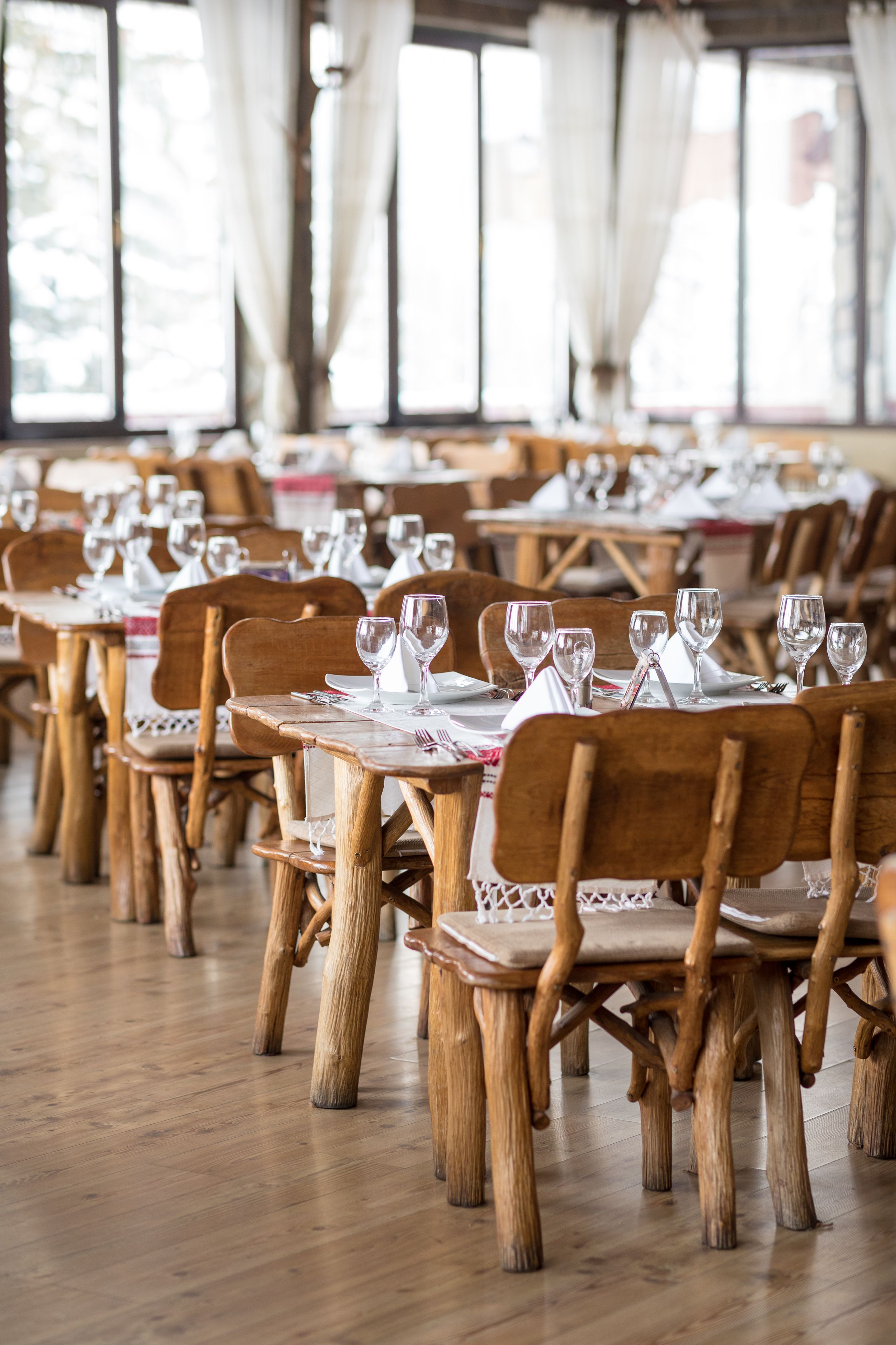 A restaurant with wooden tables and chairs, arranged in rows.
