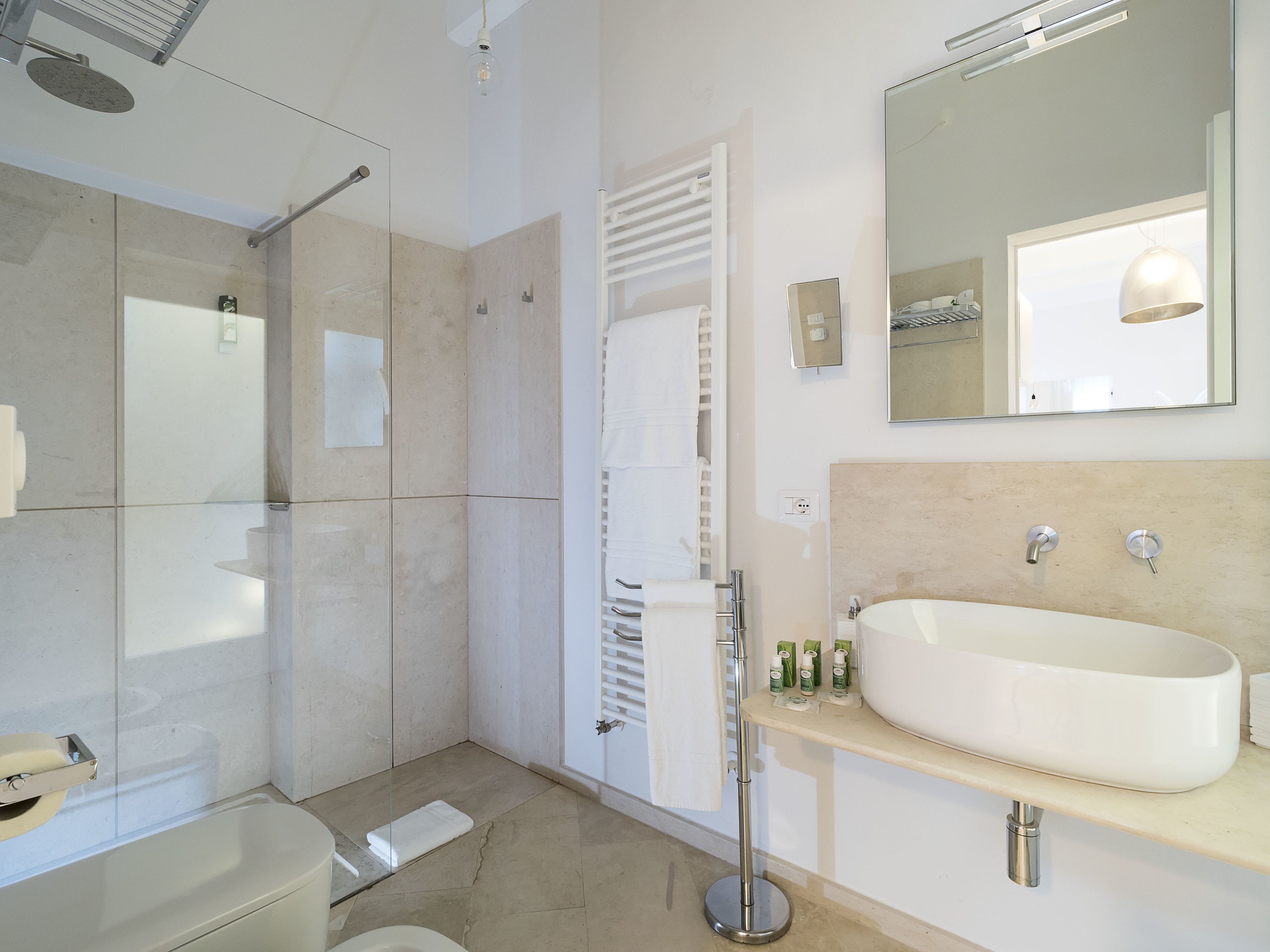 A modern bathroom with a glass-enclosed shower, a large mirror, and a beige-tiled floor.