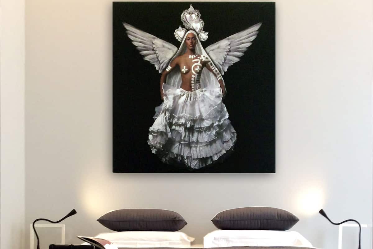 A bedroom with a bed, pillows, and a wall-mounted artwork of a figure with wings.