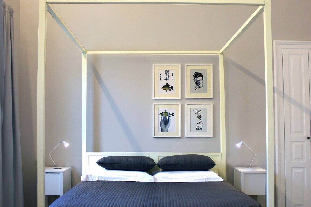 A modern bedroom with a four-poster bed, bedside tables, and framed artwork on the wall.