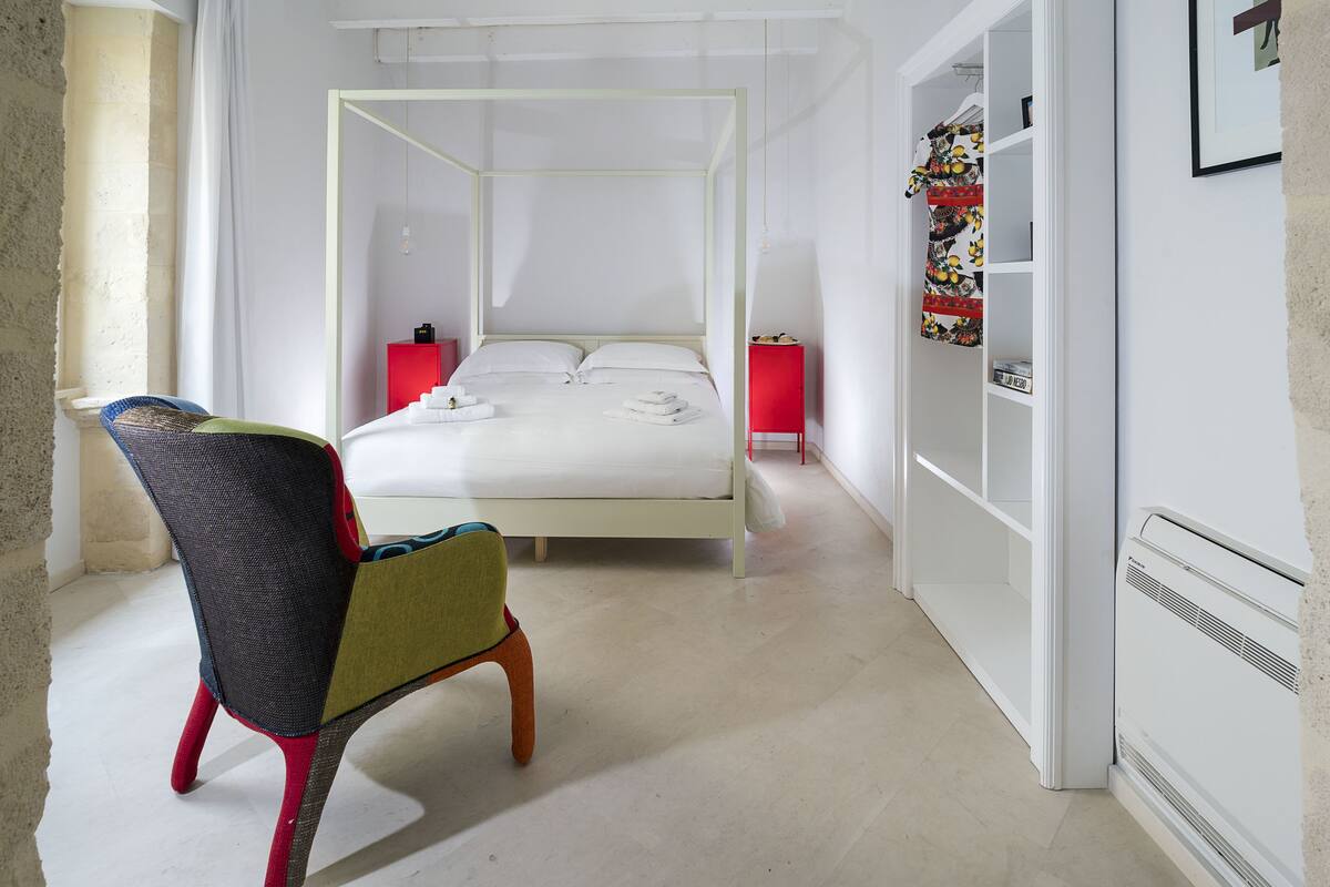 A bedroom with a four-poster bed, a red nightstand, a wardrobe, and a chair.