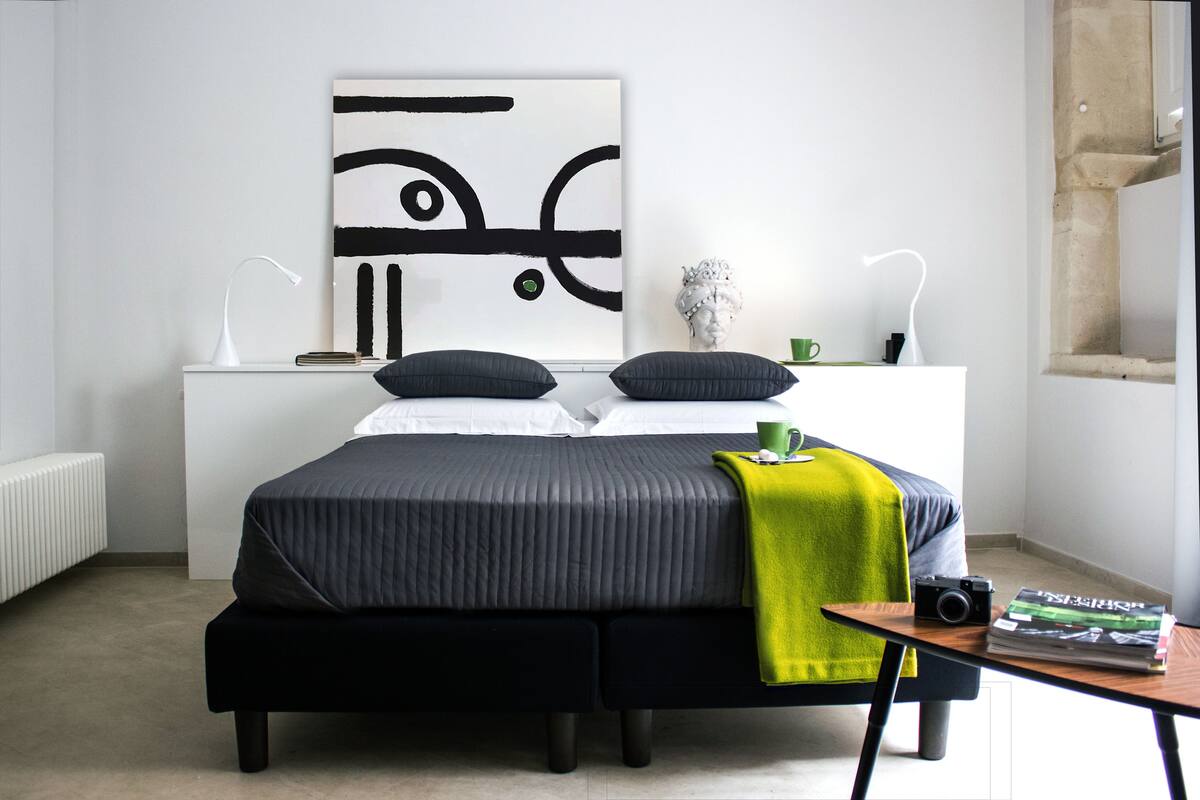 A modern bedroom with a bed, bedside table, and a wall-mounted abstract artwork.