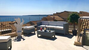 A rooftop terrace with a white sofa, two white chairs, a small table with a drink and glasses, and a cactus sculpture. - Re Federico Boutique Hotel (Syracuse)