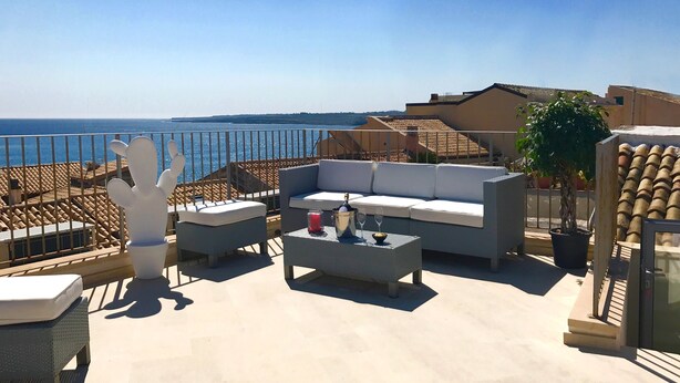 A rooftop terrace with a white sofa, two white chairs, a small table with a drink and glasses, and a cactus sculpture. - Re Federico Boutique Hotel (Syracuse)