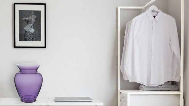 A white room with a purple vase, a framed picture, and a white shirt hanging on a rack. - Re Federico Boutique Hotel (Syracuse)