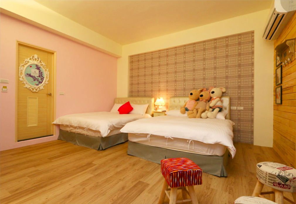A bedroom with two beds, a wooden floor, a small stool, and a teddy bear on the bed.