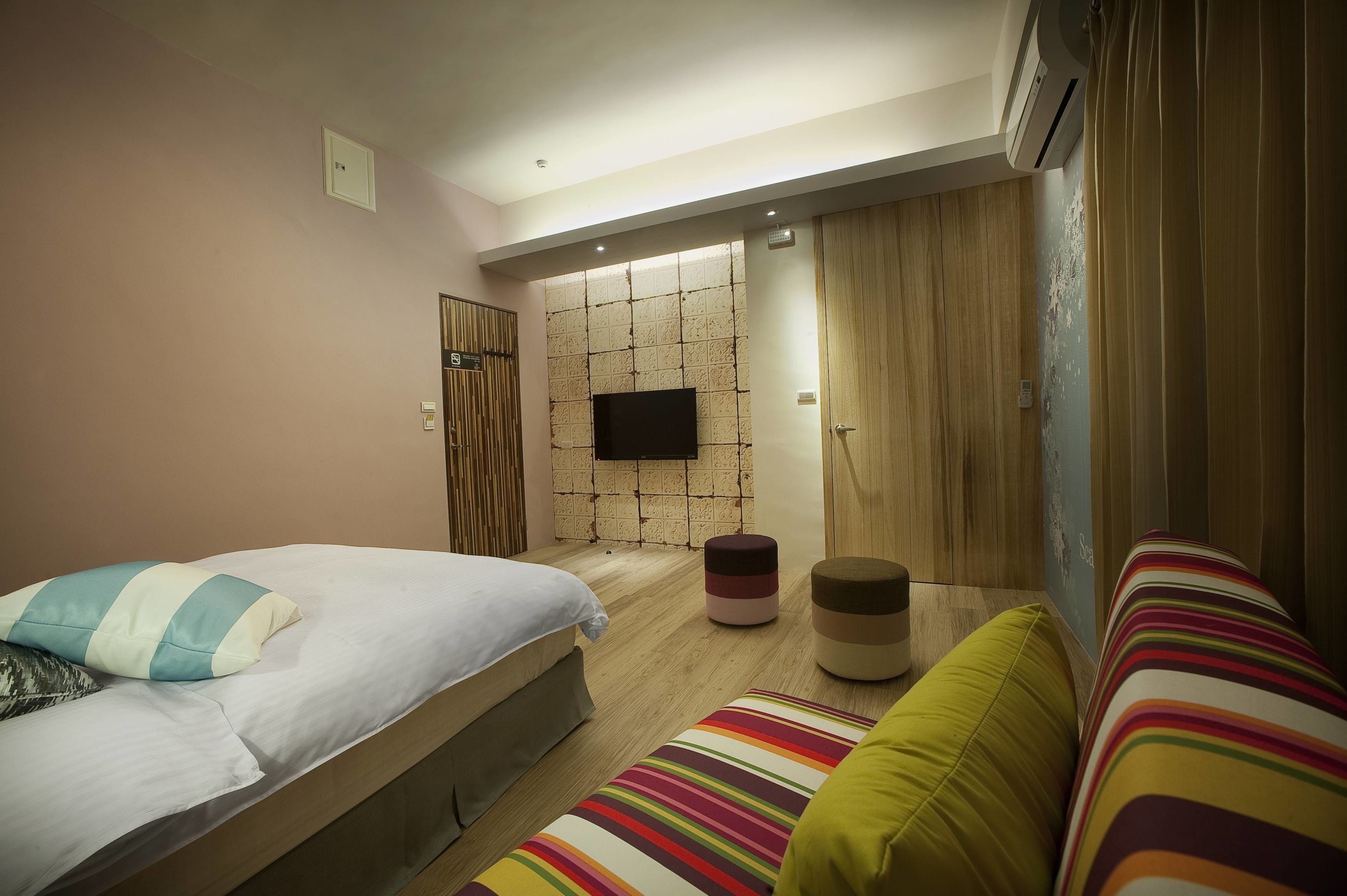 A modern bedroom with a bed, a sofa, a small ottoman, and a wall-mounted TV.