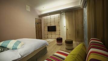 A modern bedroom with a bed, a sofa, a small ottoman, and a wall-mounted TV.