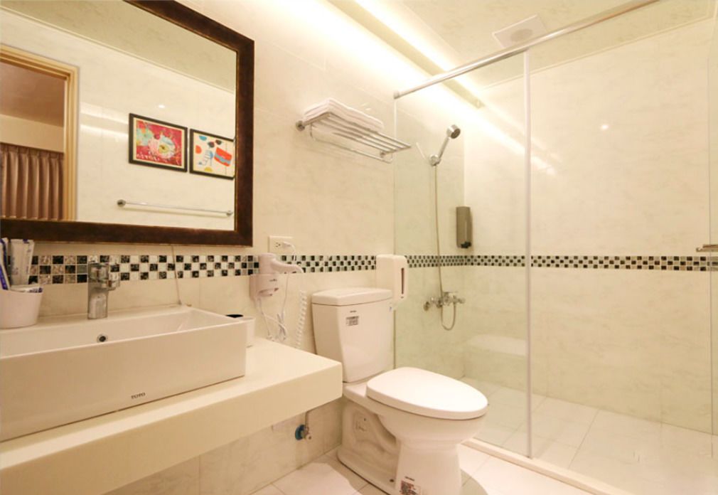 Un baño moderno con un espejo grande, un lavamanos blanco, un inodoro y una zona de ducha con mampara de vidrio.