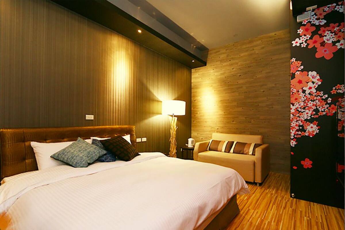 A hotel room with a large bed, a bedside table, a lamp, and a sofa.