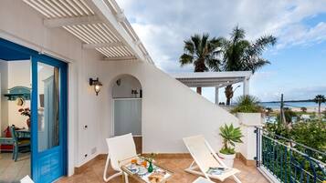 A balcony with two white lounge chairs, a small table with a tray of food and drinks, and a view of the beach.