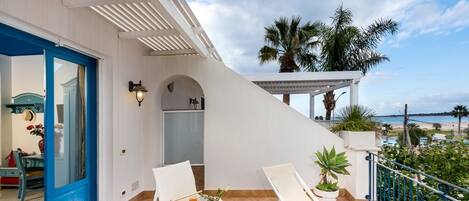 Ein Balkon mit zwei weißen Liegestühlen, einem kleinen Tisch mit einer Platte mit Essen und Getränken und Blick auf den Strand.