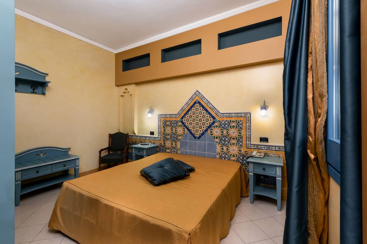 A hotel room with a bed, a chair, a nightstand, a desk, and a wall with decorative tiles.
