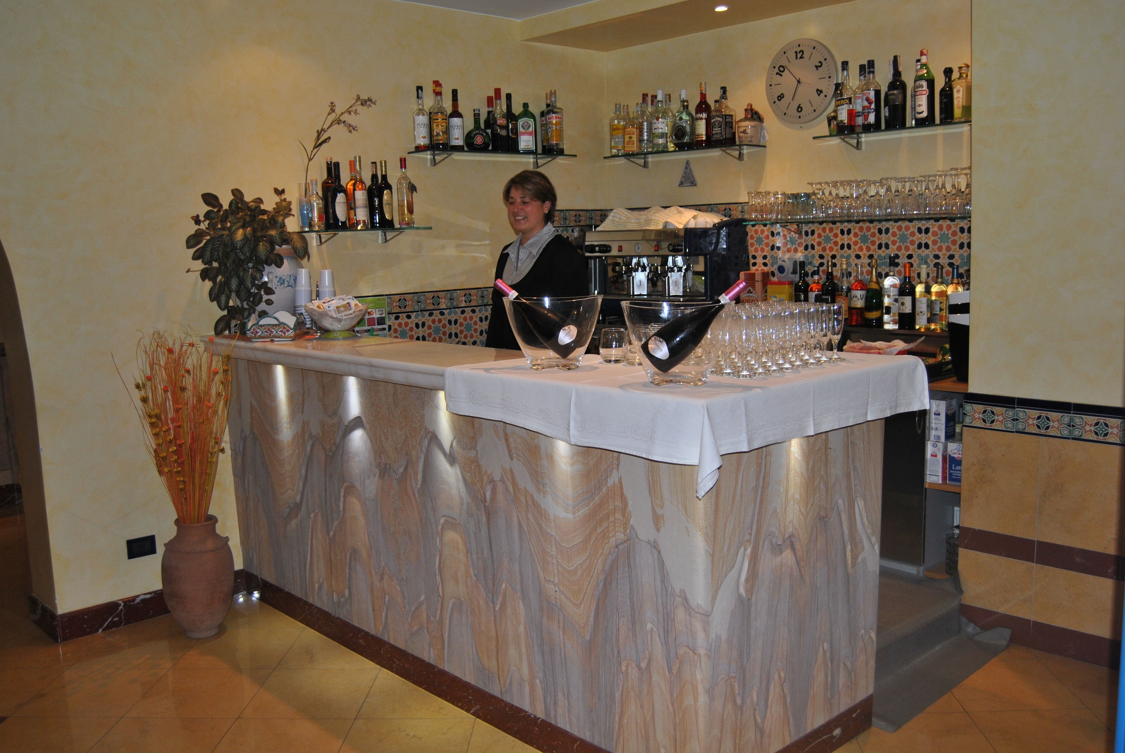 A bar area with a marble countertop, a clock, and shelves with bottles and glasses.
