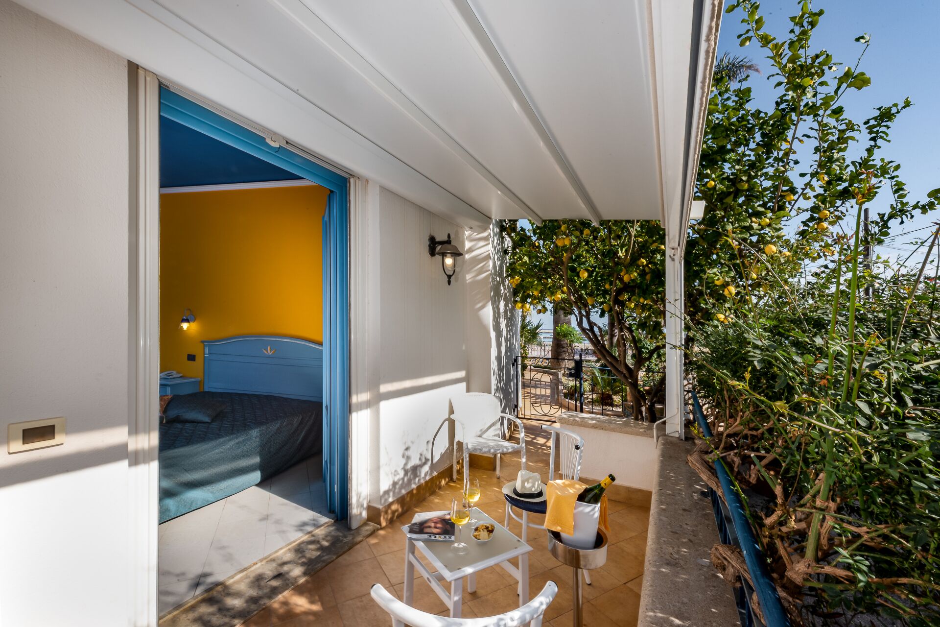 A balcony with a bed, a table with drinks, and a view of trees.