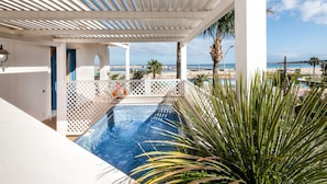 A pool area with a view of the beach, white columns, and a palm tree. - Hotel Ristorante Mediterraneo Faro (San Vito Lo Capo)