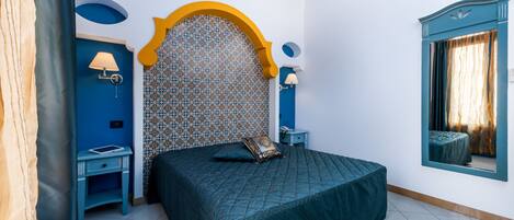A bedroom with a bed, a nightstand, a lamp, a mirror, and a window with curtains.