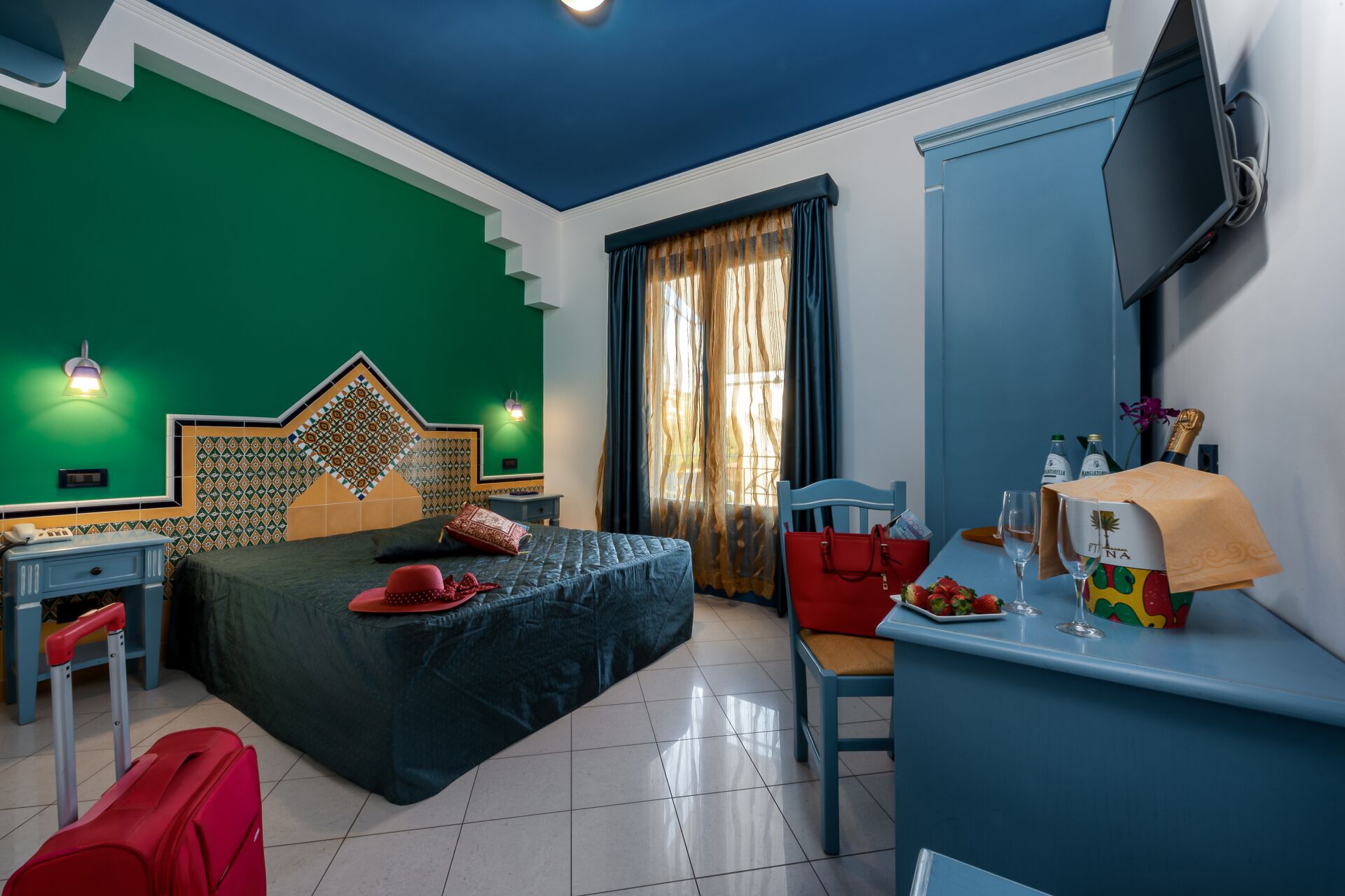 A hotel room with a bed, a desk, a chair, a TV, and a window with curtains.