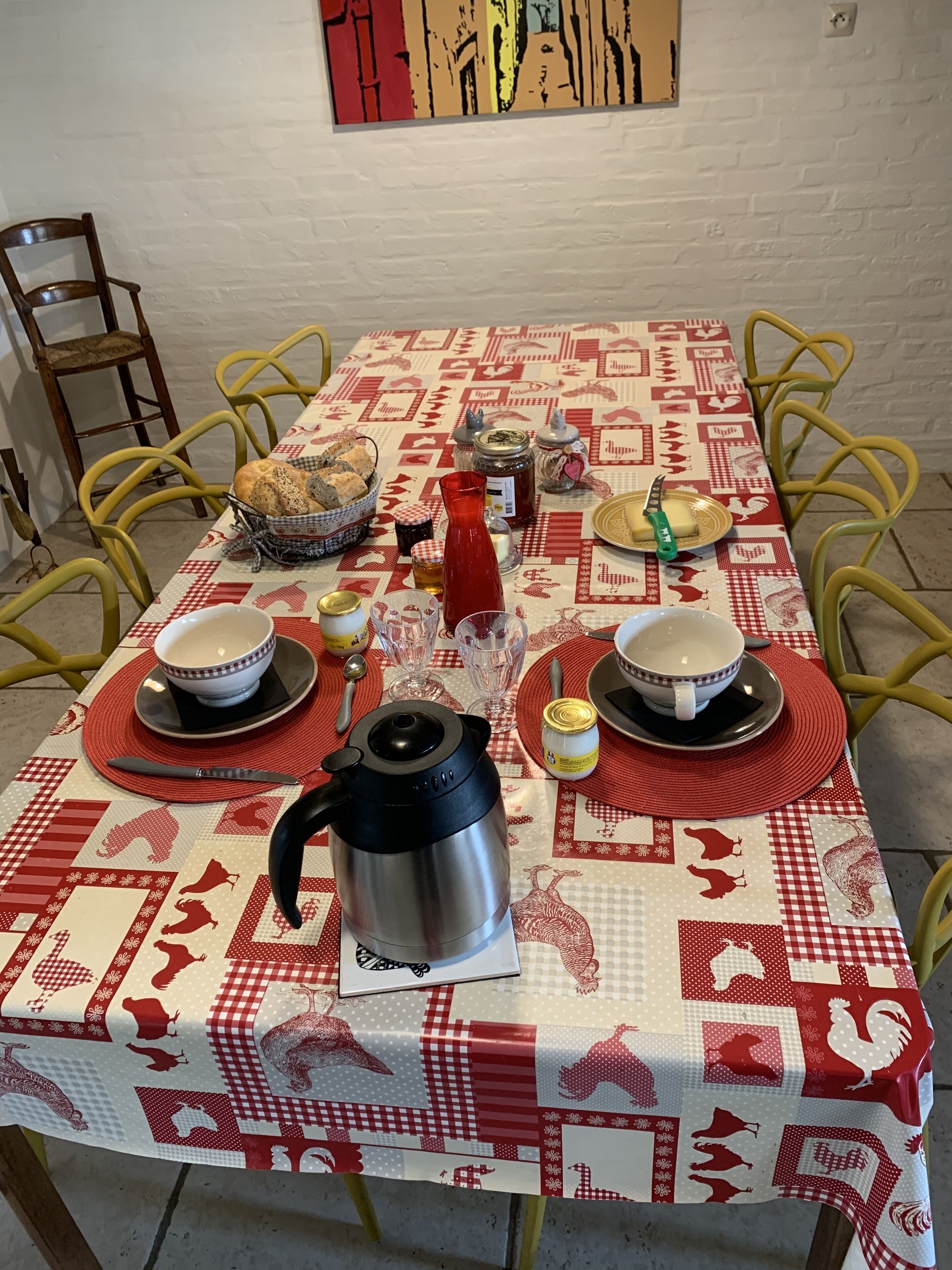 Une table à manger dressée avec une nappe à carreaux rouges et blancs, différents plats, un pichet rouge et une théière en argent.