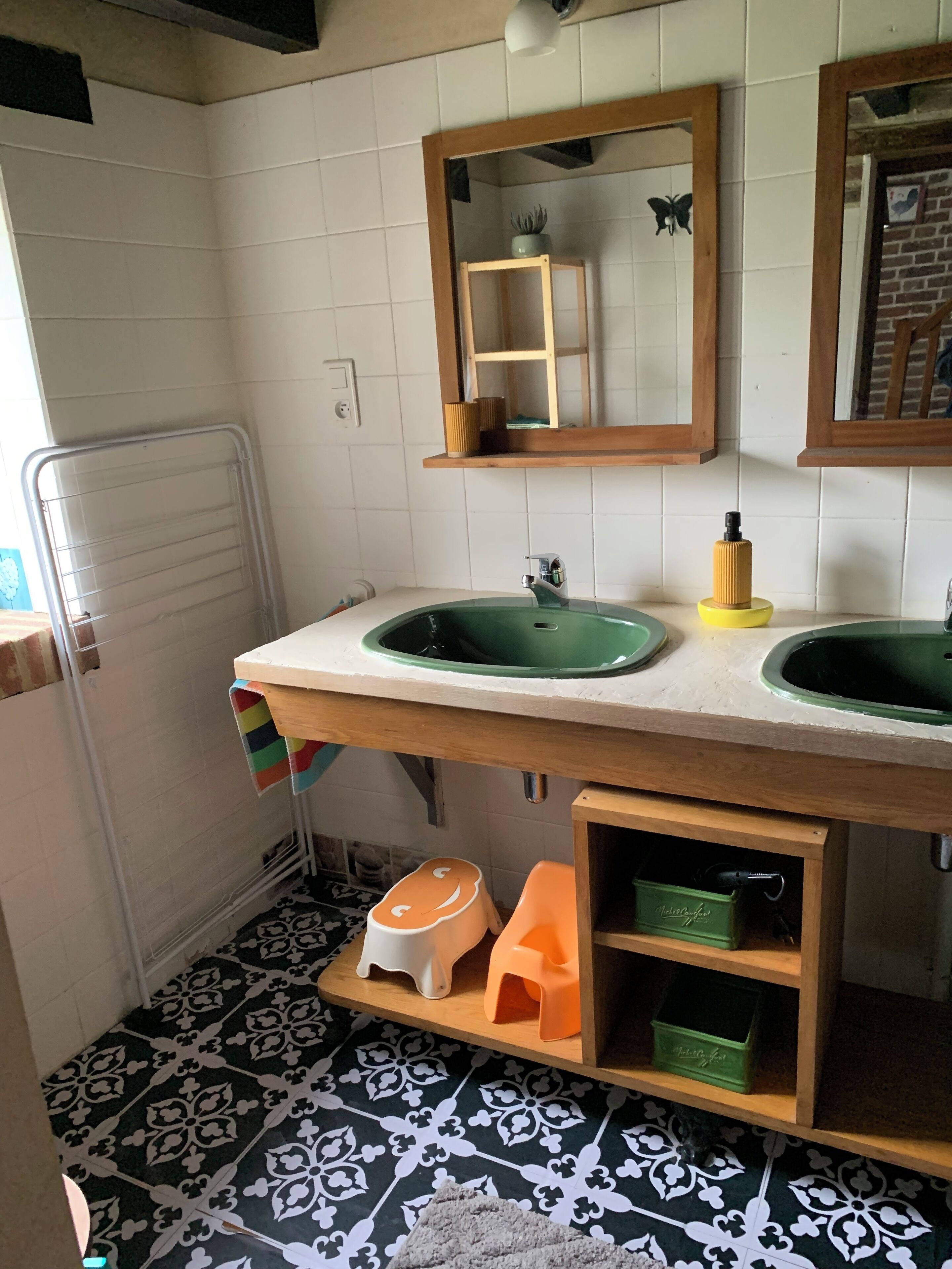 Un baño con dos lavamanos, un espejo, toallero, radiador y baldosas de suelo con diseño.