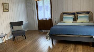 A bedroom with a wooden floor, a bed with blue bedding, a chair, a hanging light fixture, and a door with a window.
