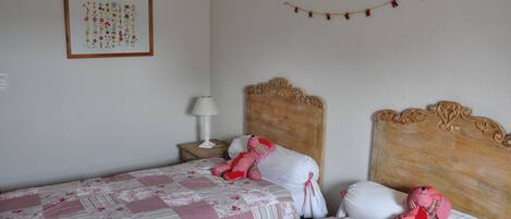 A bedroom with two beds, each with floral bedding and a teddy bear on one of the beds.