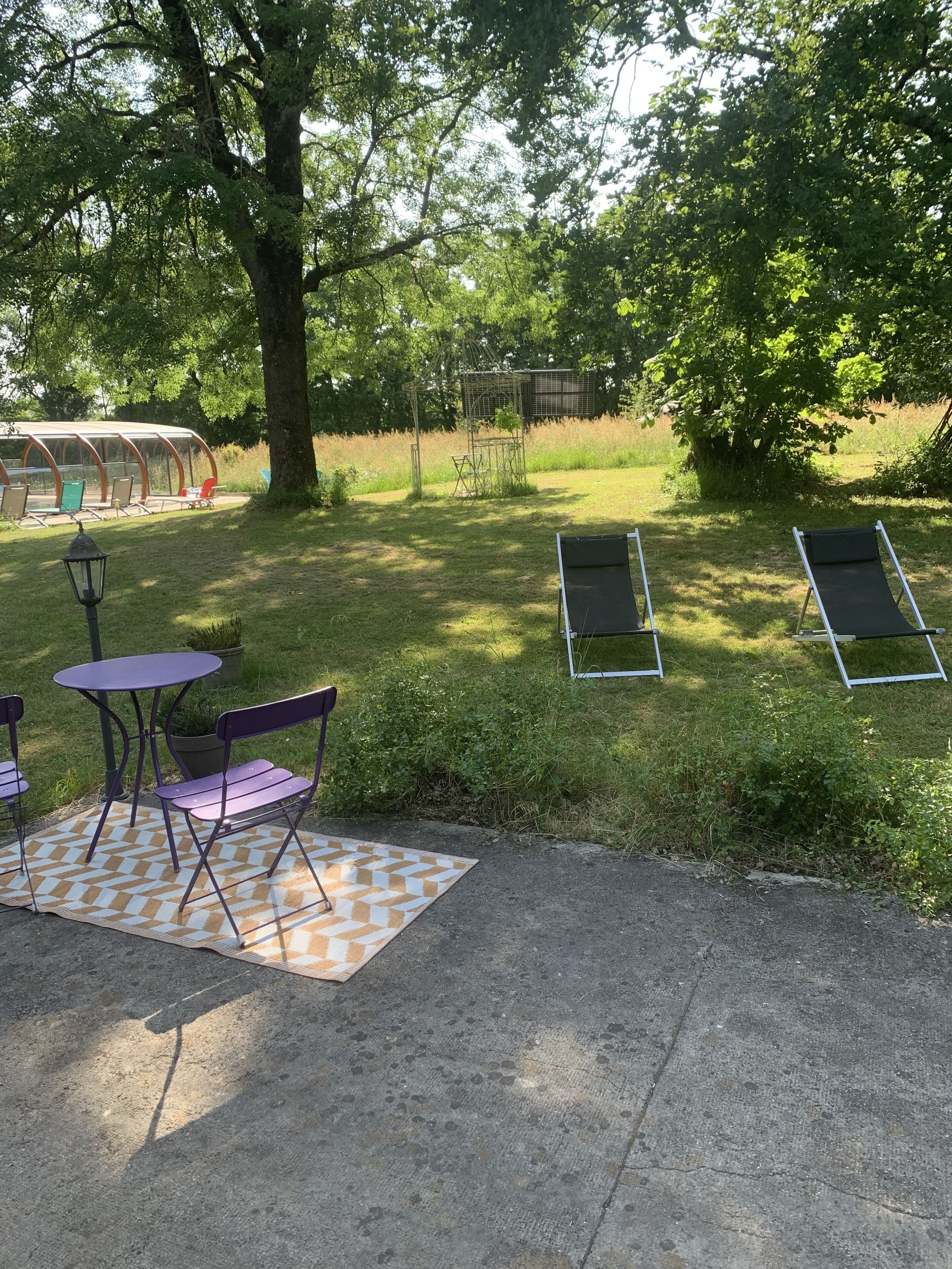 An outdoor seating area with a table and chairs, a covered seating area, and a grassy lawn.