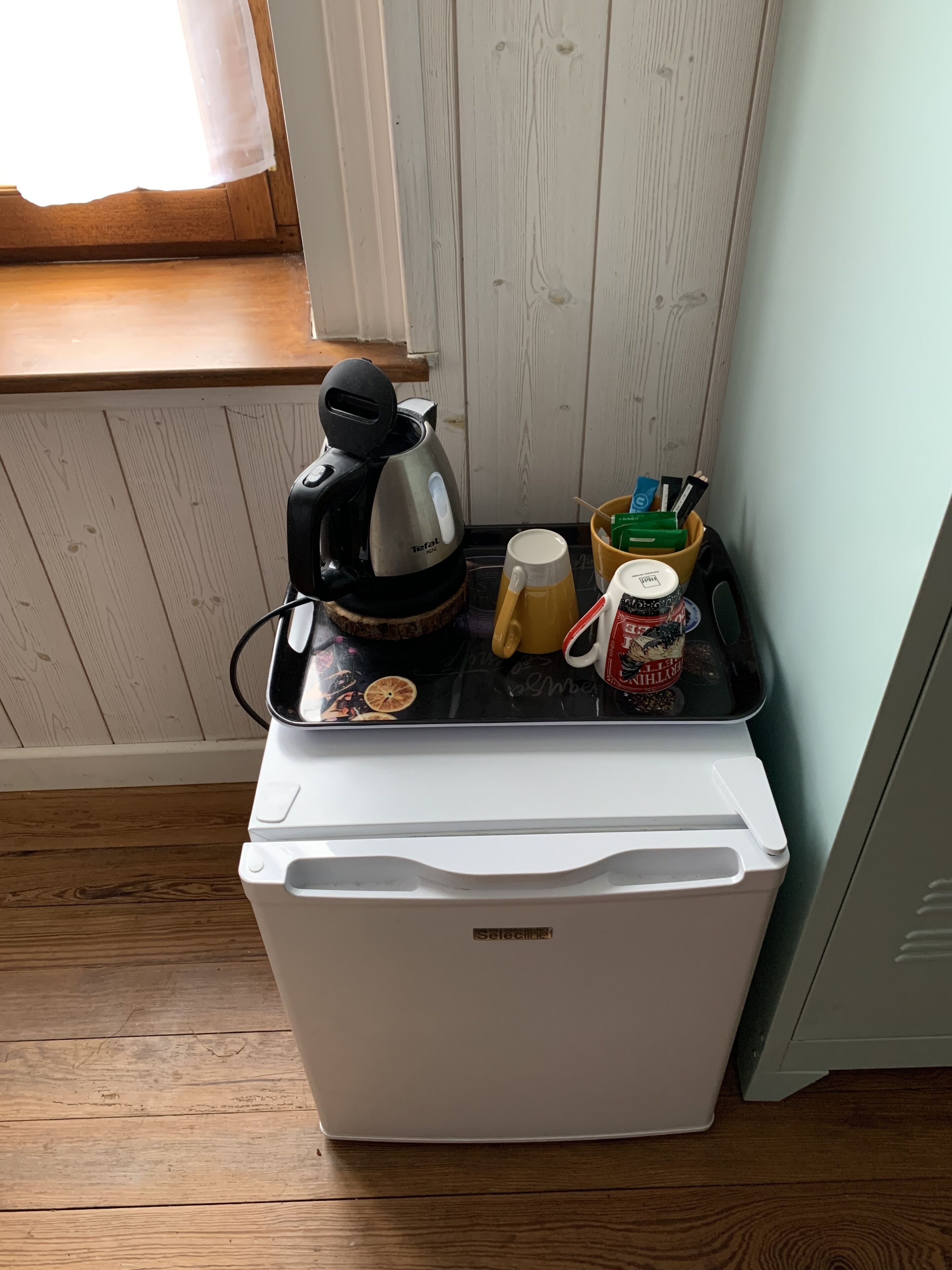 Un refrigerador compacto con un café, una taza y un recipiente con condimentos encima.