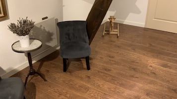 A room with a wooden floor, a grey upholstered chair, a small white table with a plant, and a white door.