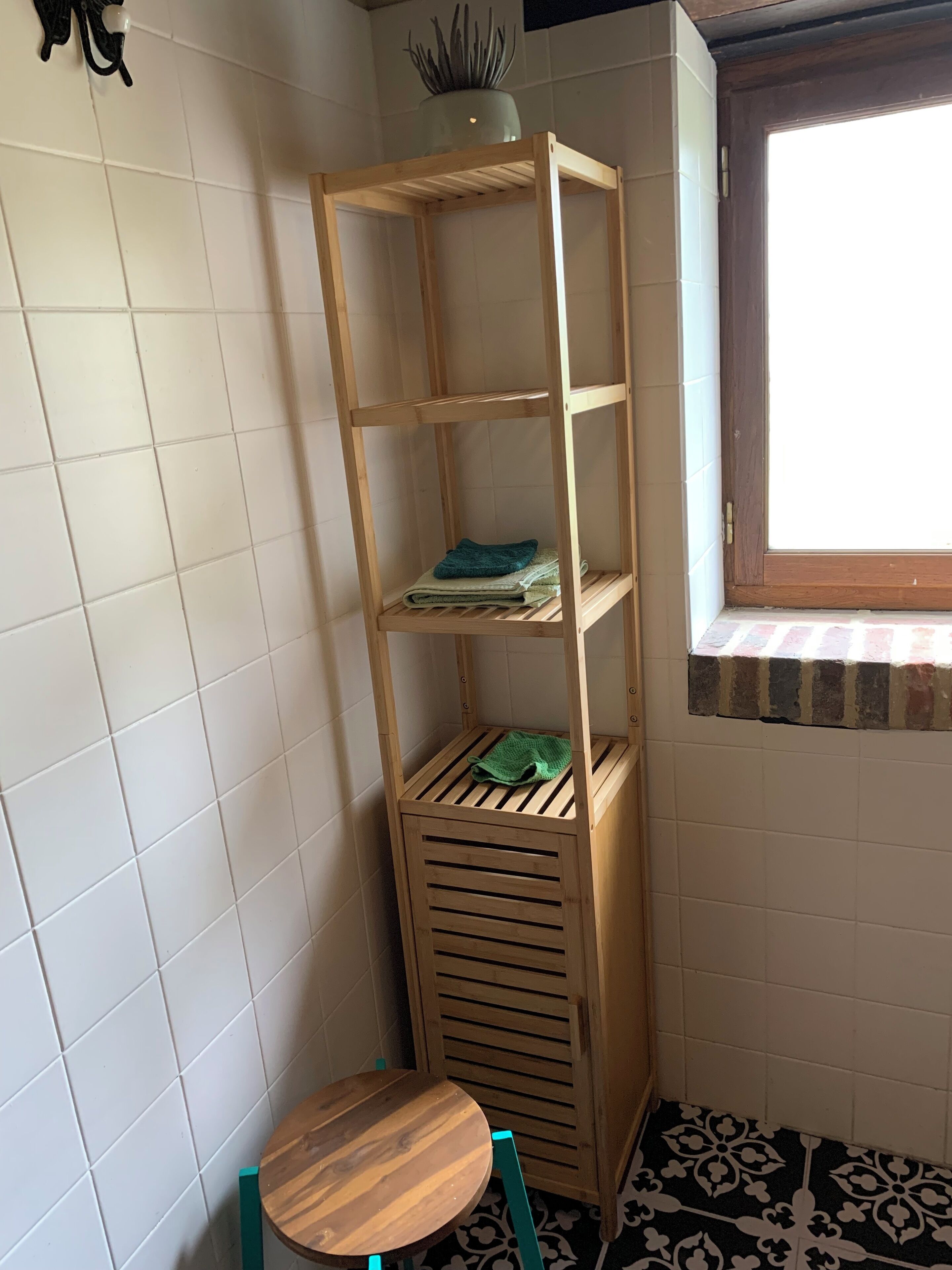 A corner room with a wooden shelf unit, a small round table, and a window with a view.