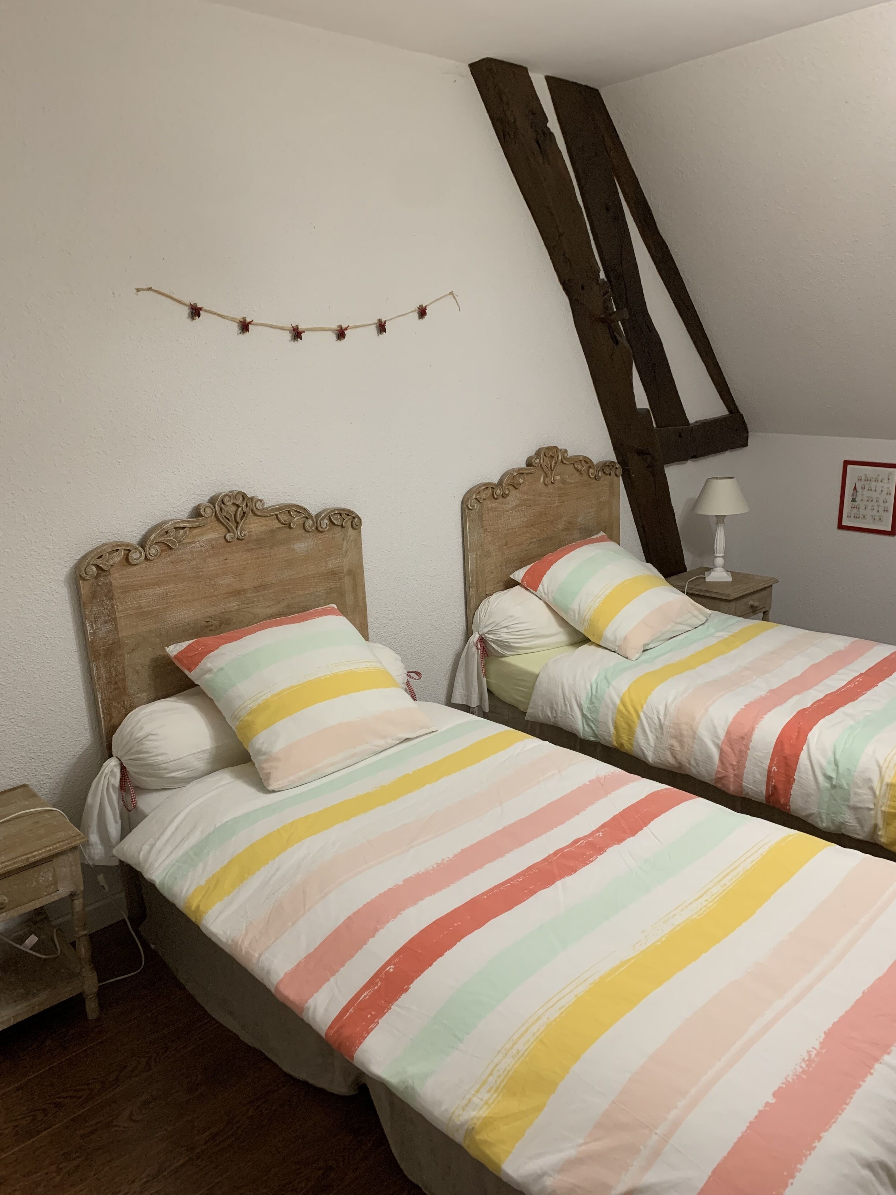 Un dormitorio con dos camas individuales, cabeceros de madera, una mesita de noche pequeña, una lámpara y un cuadro colgado en la pared.